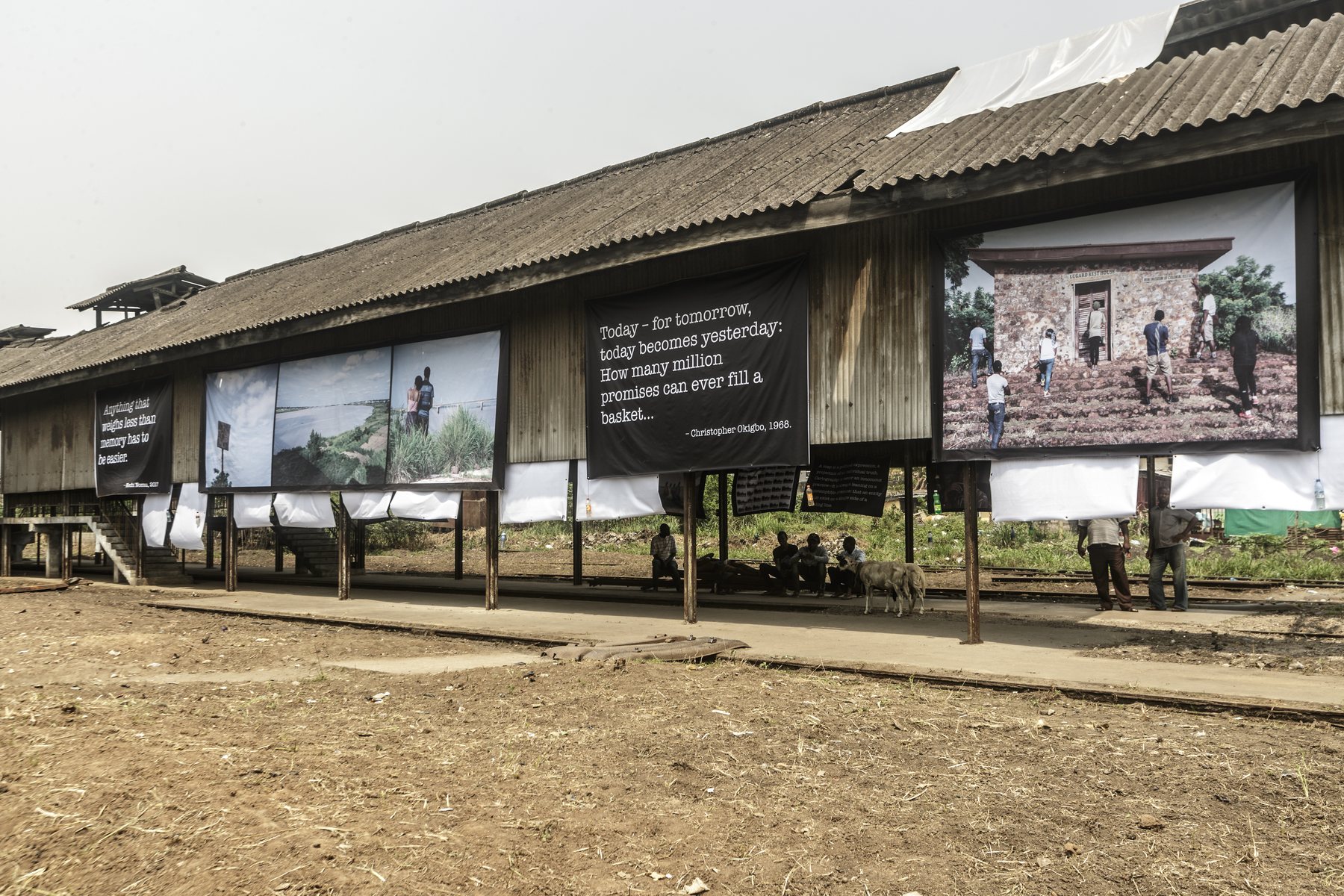 Large photographic banners hung the length of an abandoned railway shed, seen from the trackside