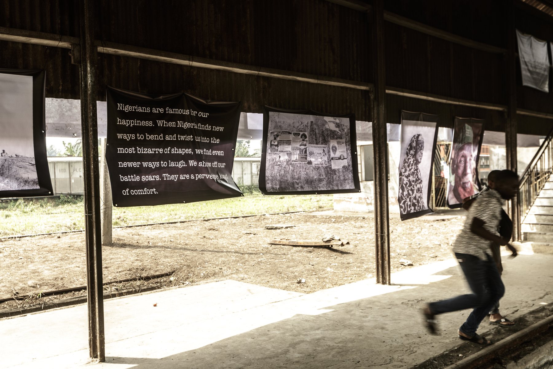 A child running past hanging photographic works and a text panel inside the railway shed