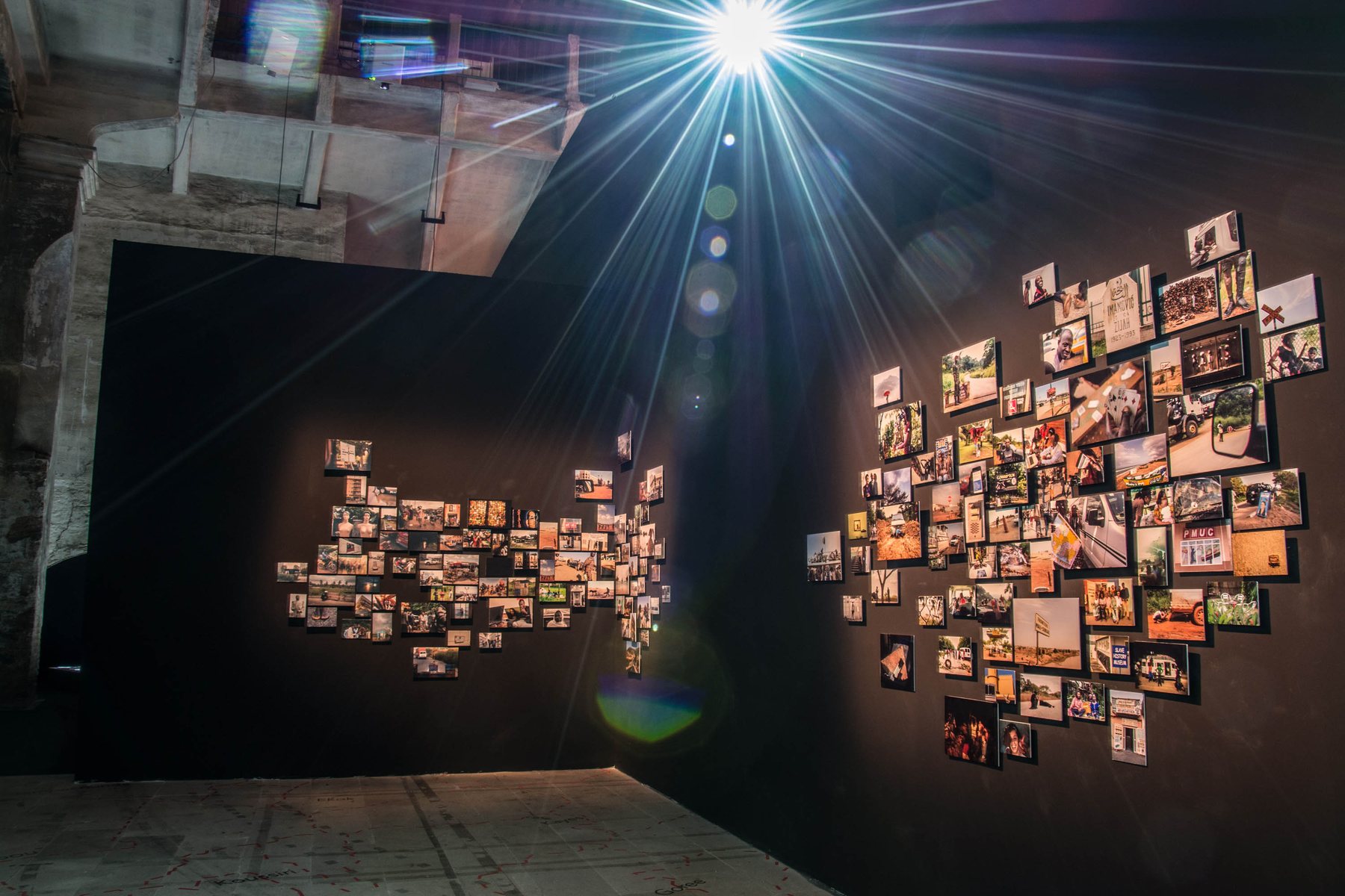 Photographs pinned across a dark wall in the Arsenale, lit from above