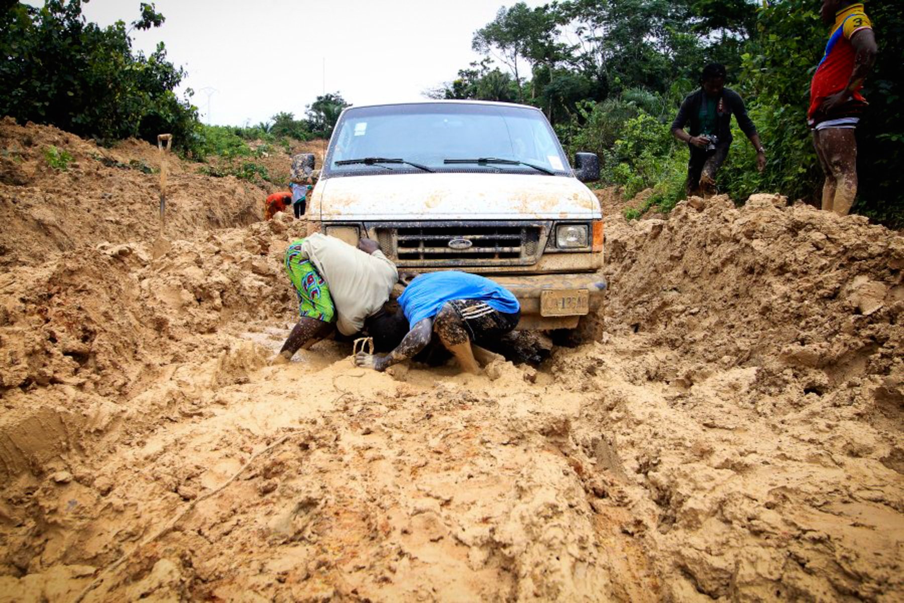 A vehicle sunk to its axles in deep mud, with participants working around it
