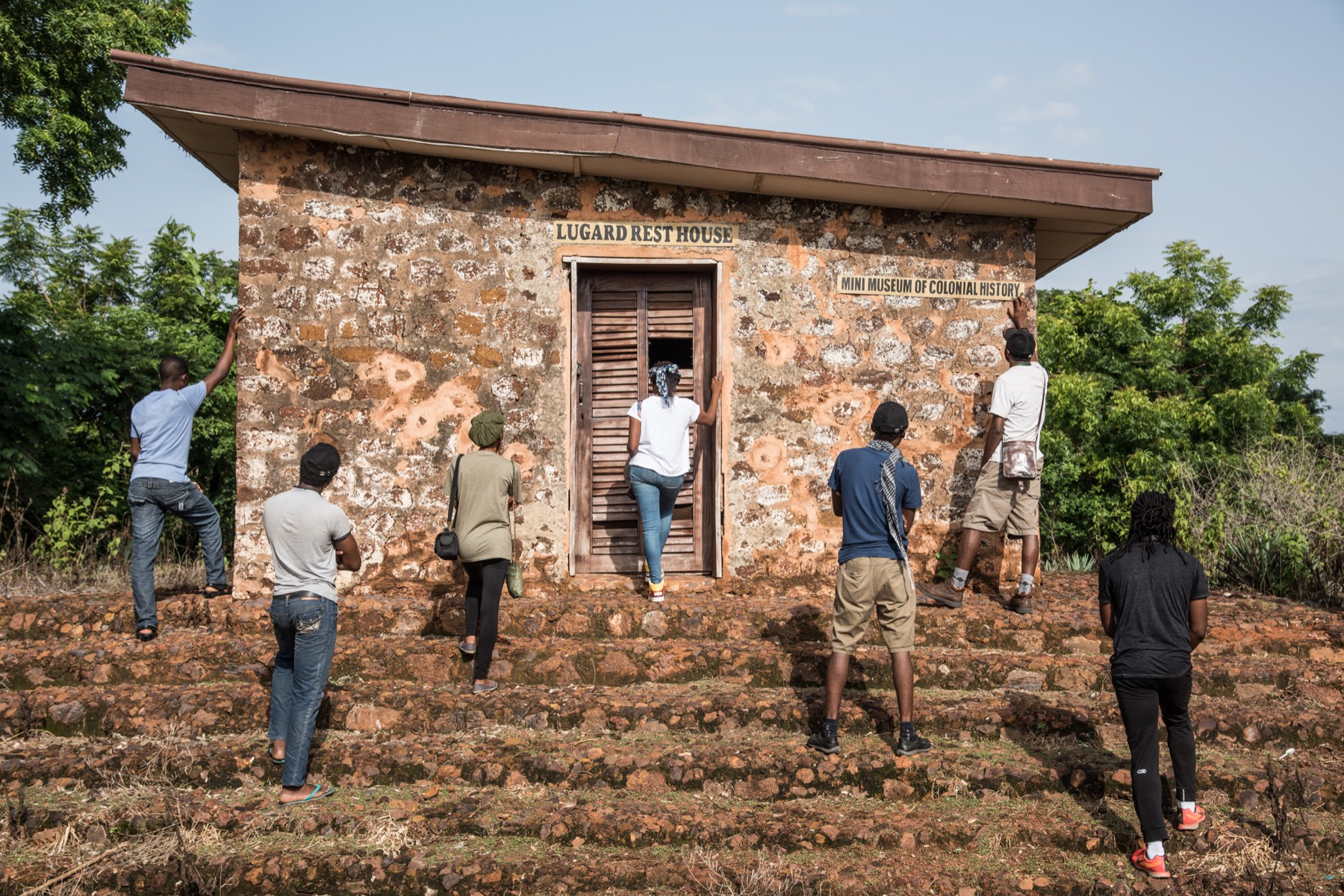 Eight participants at the wall of Frederick Lugard's rest house, one stepping through the doorway.